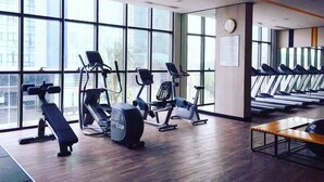 Une salle de sport équipée de divers appareils d’exercice, dotée de grandes fenêtres et d’un plancher en bois.