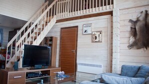 Un interior de madera con una escalera, un televisor sobre una mesa de vidrio y un sofá.