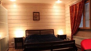Una habitación con paneles de madera, una cama, dos lámparas de noche, un sillón rojo y un ventanal con cortinas.