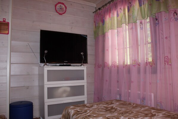 A bedroom with a bed, a TV on a white cabinet, and pink curtains with cartoon characters. - Villa Viktoriya (Ruokolahti)