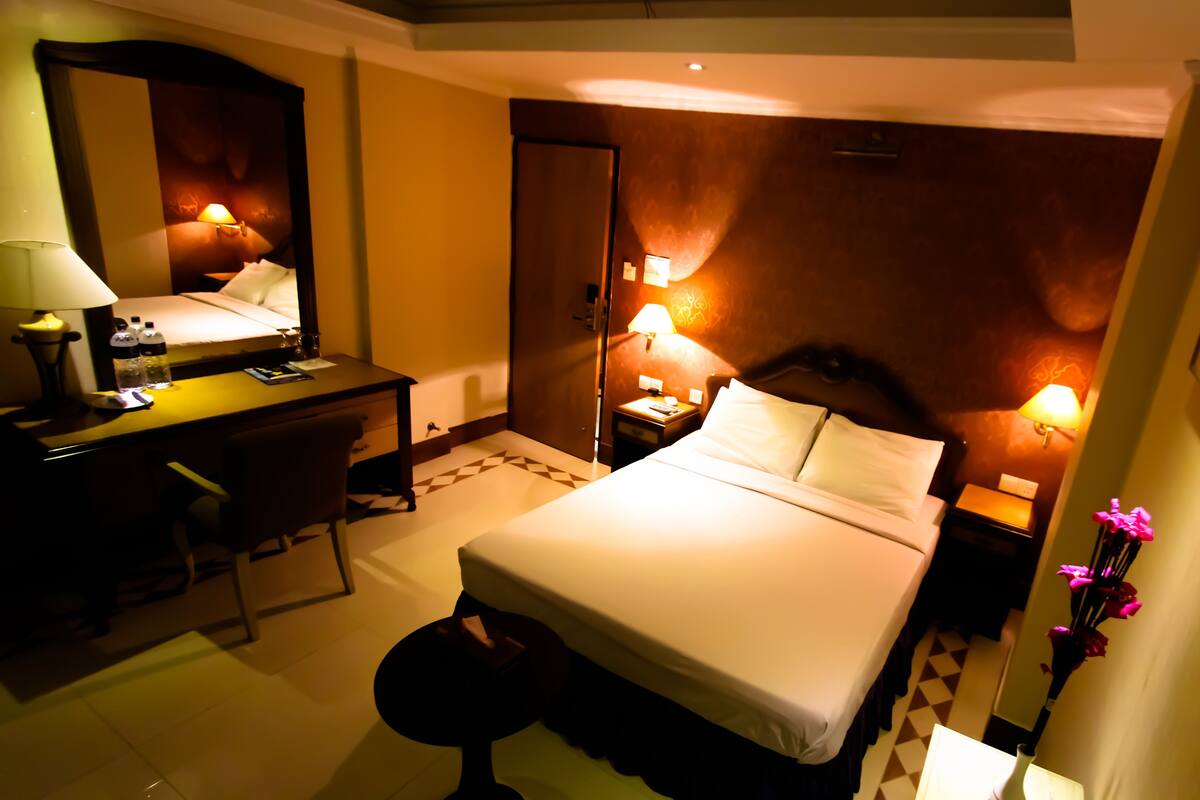 A hotel room with a bed, desk, chair, bedside tables, lamps, and a mirror.