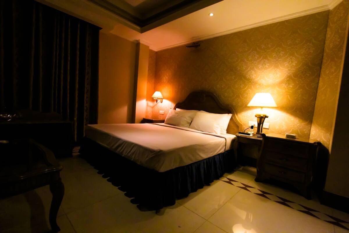 A hotel room with a bed, two bedside lamps, a nightstand, a dresser, and a chair.