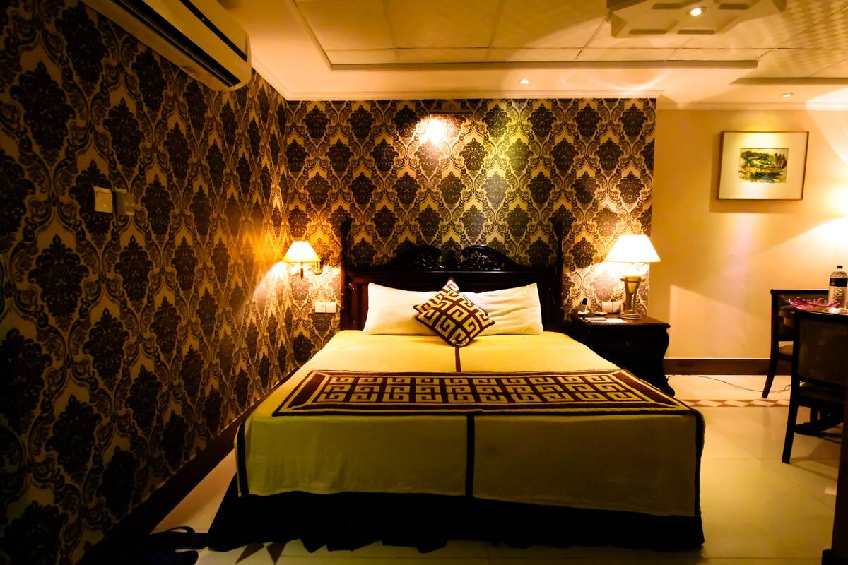 A hotel room with a large bed, two bedside lamps, patterned wallpaper, and a framed picture on the wall.