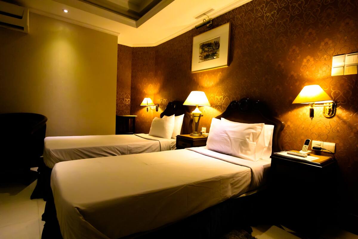 A hotel room with two beds, bedside lamps, a nightstand with a phone, and a framed picture on the wall.