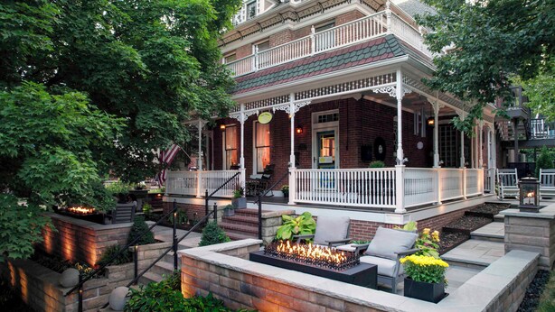 A two-story brick house with a covered porch, outdoor seating, and a fire feature. - Main Street Inn (Parkville)