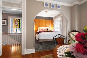 A bedroom with a wooden headboard, a bed with white bedding, a nightstand, and a window with a stained glass design. - Main Street Inn (Parkville)