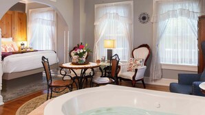 A room with a bed, a sitting area with a table and chairs, a bathtub, and large windows with curtains. - Main Street Inn (Parkville)