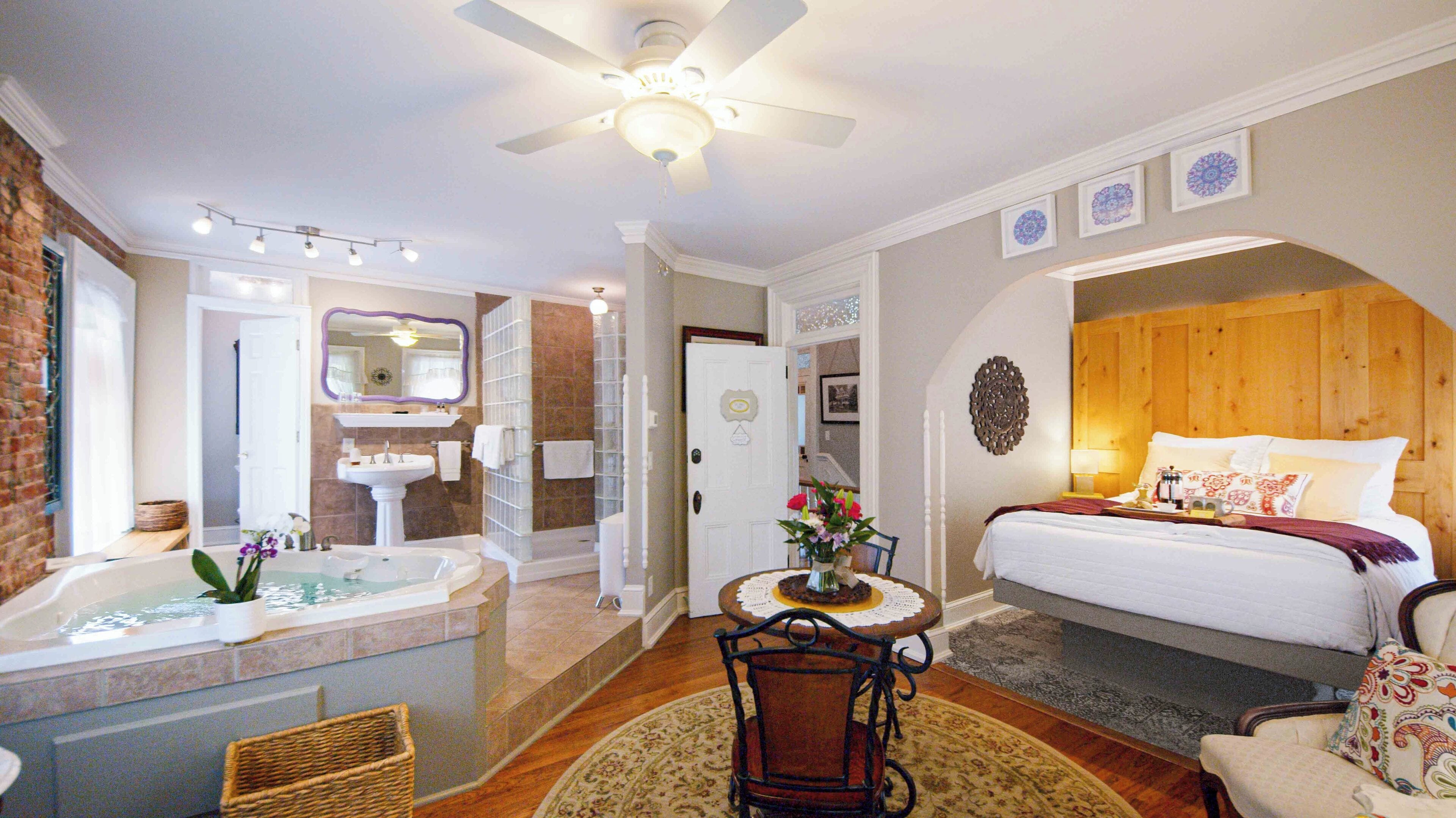 A hotel room with a large bed, a sitting area with a table and chairs, a bathroom with a bathtub, and a ceiling fan.