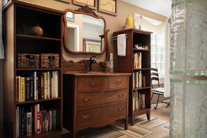 A wooden dresser with drawers, a mirror, and a bookshelf filled with books. - Main Street Inn (Parkville)