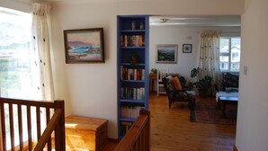 A living room with a wooden floor, a blue bookshelf, a painting, a chair, and a window with curtains. - Dreams (Pringle Bay)