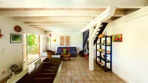 Amplia sala de estar con sofá, una mesita de centro y una estantería. Una escalera conduce a un nivel superior.