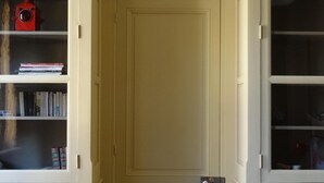 Een kamer met een gesloten deur, witte paneelwanden en een houten vloer.