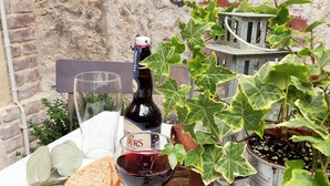 A table with a bottle of wine, a glass of wine, a plate with cheese and bread, and a potted plant. - MY LITTLE GARDEN - Garden - Free parking 600m - La Clé de Honfleur (Honfleur)