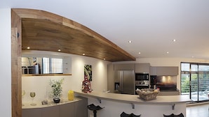 A modern kitchen with a curved wooden ceiling, stainless steel appliances, and a large window overlooking a balcony.