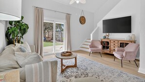 A spacious living room with a large TV, a staircase, and a view of the outdoors. -  Island Breeze in Vilano Beach Peaceful Getaway (Jacksonville)