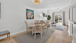 A dining area with a round table and chairs, a chandelier, and a painting of flowers on the wall.
