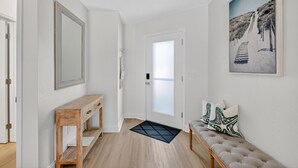 A hallway with a wooden console table, a bench with patterned cushions, a large framed picture on the wall, and a door with frosted glass. -  Island Breeze in Vilano Beach Peaceful Getaway (Jacksonville)