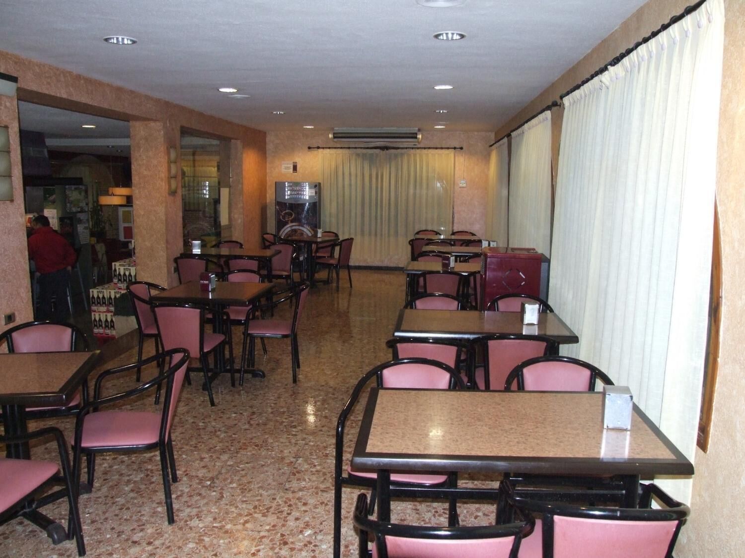 A restaurant with multiple tables and chairs, a tiled floor, and a large window with curtains.