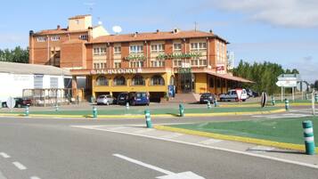 A hotel with a bar and restaurant on the ground floor, multiple parking spaces, and a clear road in front.