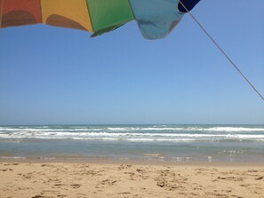 Une plage avec un parasol coloré et une vue dégagée sur l’océan.