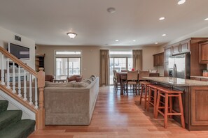 A spacious living area with a large sofa, a dining table with chairs, and a kitchen with a refrigerator and wooden cabinets.