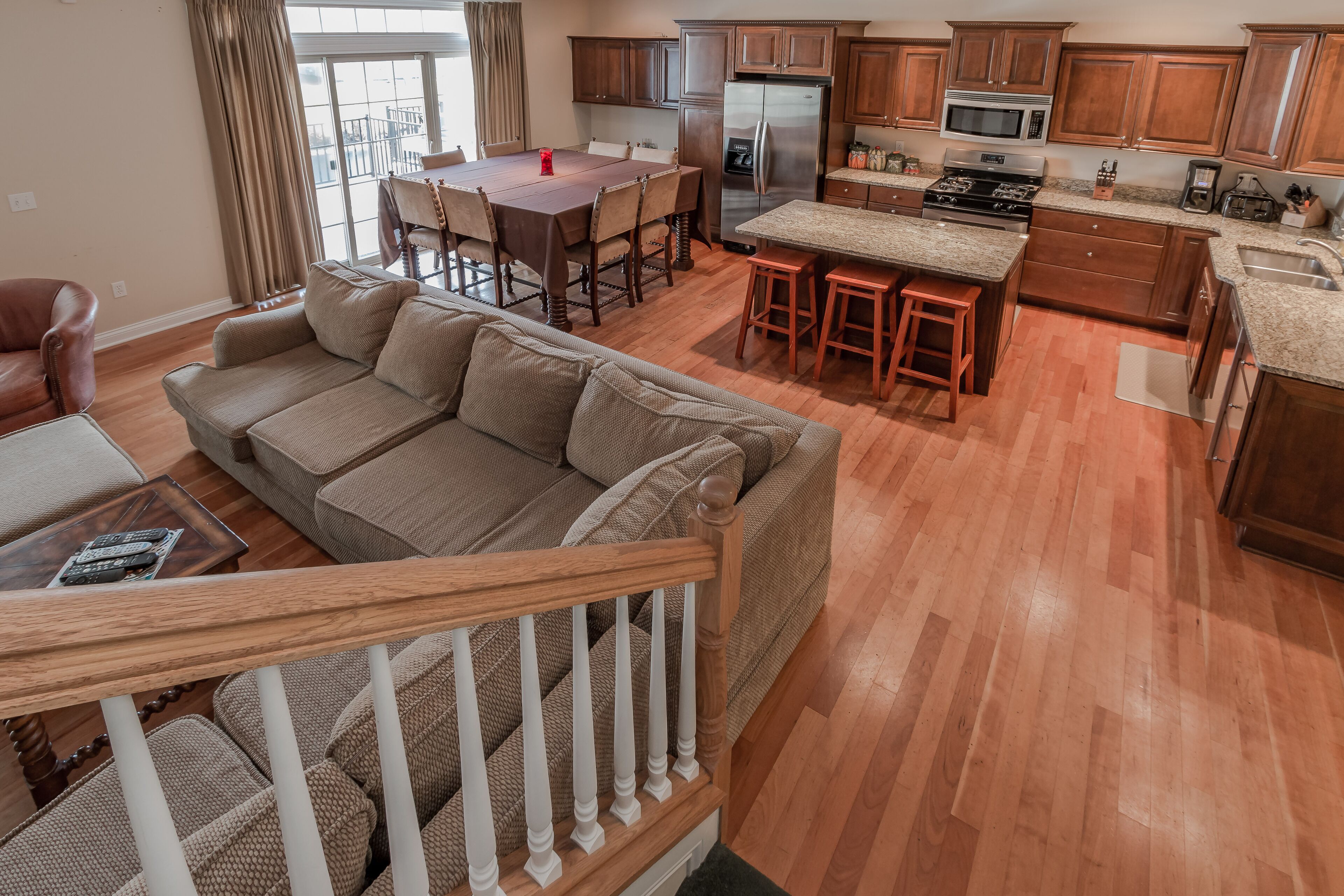 A spacious living room with a large brown sofa, a dining table, and a kitchen area with wooden cabinets and stainless steel appliances.