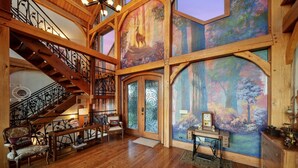 Ein geräumiges Foyer mit einer Holztreppe, einer großflächigen Wandmalerei von Waldlandschaft und einem alten Schreibtisch mit Lampe.