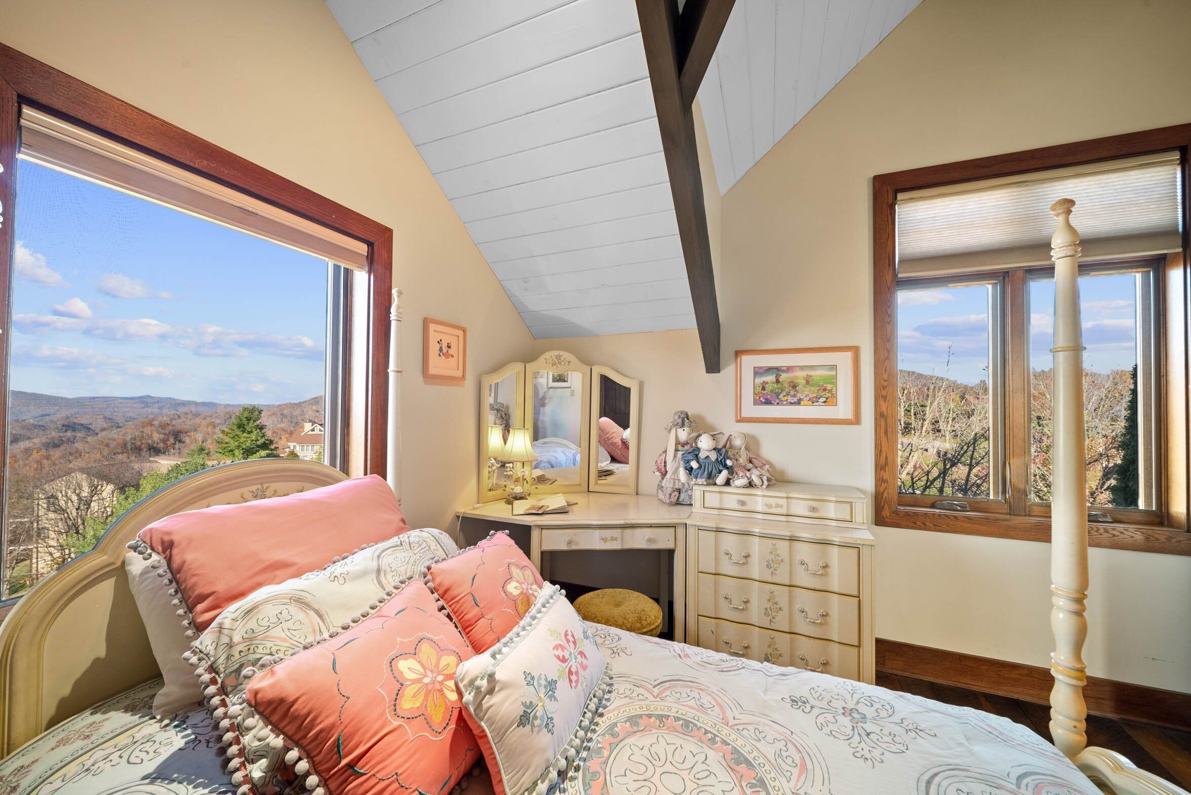 A bedroom with a bed, dresser, and a large window with a view of the outdoors.