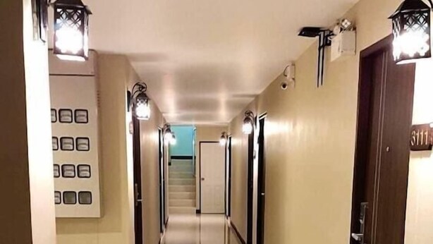A long, well-lit hallway with a tiled floor, doors on the right, and wall-mounted lights.