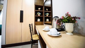 A compact kitchen with wooden cabinets, a black kettle, and a white mug on the counter.
