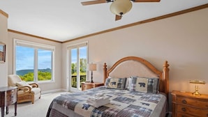 Une chambre avec un grand lit, un ventilateur de plafond, une chaise, une table de chevet et une vue sur l’extérieur.
