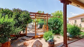 Ein überdachter Patio-Bereich mit einer Holz-Pergola, Sitzgelegenheiten und Pflanzen in Töpfen.