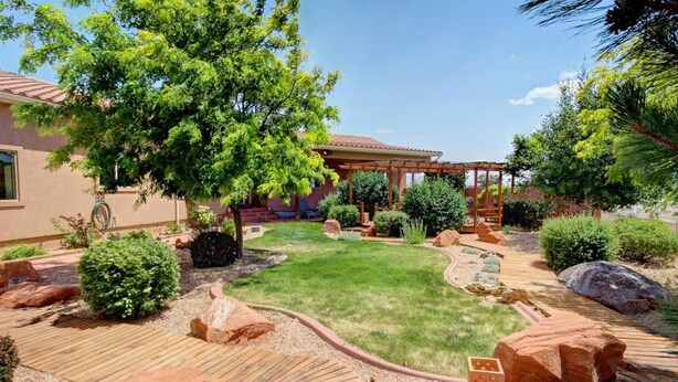 Ein gepflegter Garten mit einer Holzterrasse, einer Pergola und verschiedenen Sträuchern und Bäumen.