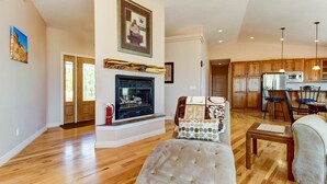 Ein geräumiges Wohnzimmer mit Holzböden, einem Kamin und einem Essbereich mit Holzsäulen sowie einer Küche im Hintergrund.