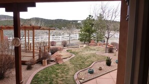 Ein Terrassenbereich mit einer Pergola, einer Holzdielenveranda und einem angelegten Garten mit einem kleinen Baum und Topfpflanzen.