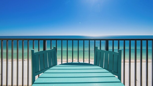 Vista desde un balcón sobre una playa con cielo despejado y mar tranquilo.