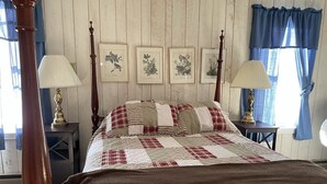 Ein Schlafzimmer mit einem hölzernen Bettgestell, einer gesteppten Bettdecke, zwei Nachttischlampen und gerahmten Pflanzenmotiven an der Wand.