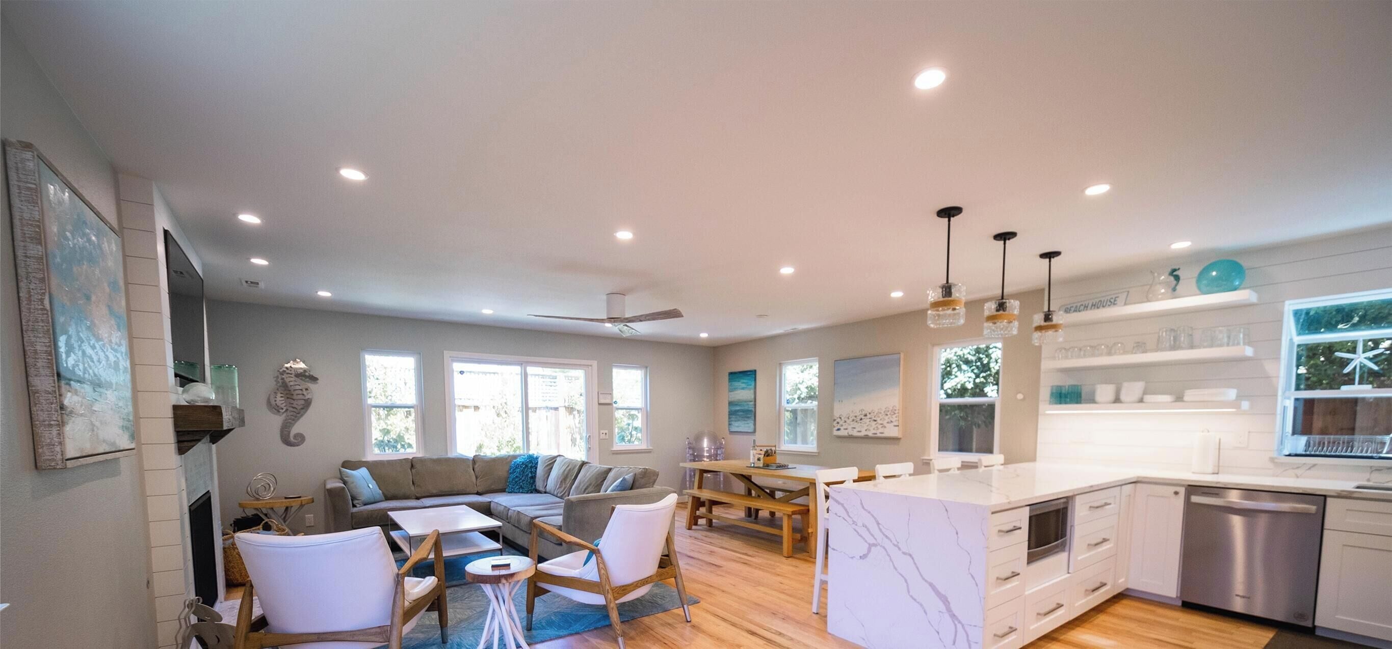 A spacious living area with a wooden floor, a sofa set, a dining table, and a kitchen with white cabinetry and a dishwasher.