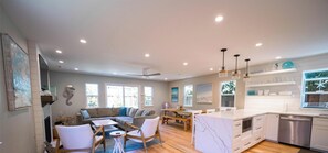 A spacious living area with a wooden floor, a sofa set, a dining table, and a kitchen with white cabinetry and a dishwasher.