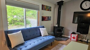 A living room with a blue sofa, a fireplace, a clock, and a television. - Private cozy cottage on Bobs Lake with boat launch (Maberly)