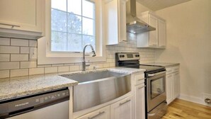 A kitchen with white cabinets, a stainless steel sink, a dishwasher, a stove, and a window with a view of trees. - A Tennessee Tiny House: A Quiet Readaway Retreat for Rest & Reconnection (Clarksville)