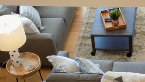 A living room with a grey sofa, a small wooden side table with a lamp, and a dark coffee table with a tray and plant. - A Tennessee Tiny House: A Quiet Readaway Retreat for Rest & Reconnection (Clarksville)
