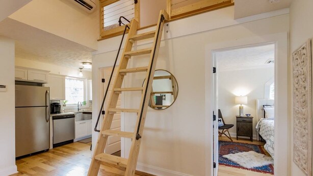 A modern kitchen with stainless steel appliances, a wooden ladder, and a view into a bedroom with a bed and a nightstand. - A Tennessee Tiny House: A Quiet Readaway Retreat for Rest & Reconnection (Clarksville)