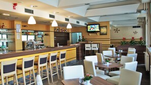Un restaurante con zona de bar, varias mesas y sillas, y un televisor en la pared.