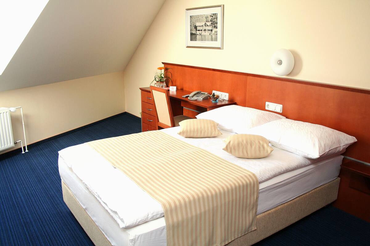 A hotel room with a large bed, a wooden headboard, a desk with a telephone, and a framed picture on the wall.