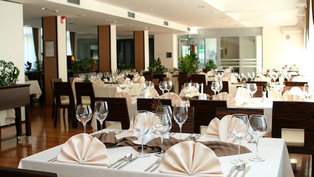 Un comedor bien iluminado con mesas dispuestas para una comida formal, con servilletas dobladas con esmero y copas de vino.