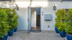 Une entrée moderne avec une porte, des plantes en pot et des luminaires fixés au mur.