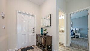 A hallway with a white door, a wooden console table with a vase and a plant, and a mirror on the wall. - (JA4907)  Home 4/3 Private Pool, Lake & Free Waterpark (Kissimmee)