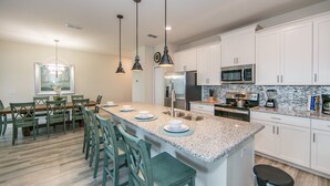 A modern kitchen with white cabinets, a granite countertop, and stainless steel appliances. There is a dining area with wooden chairs and a table. - (JA4907)  Home 4/3 Private Pool, Lake & Free Waterpark (Kissimmee)