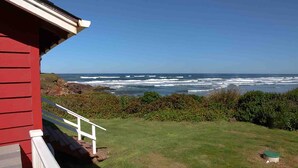 A red building with a white railing overlooking a grassy area and the ocean.